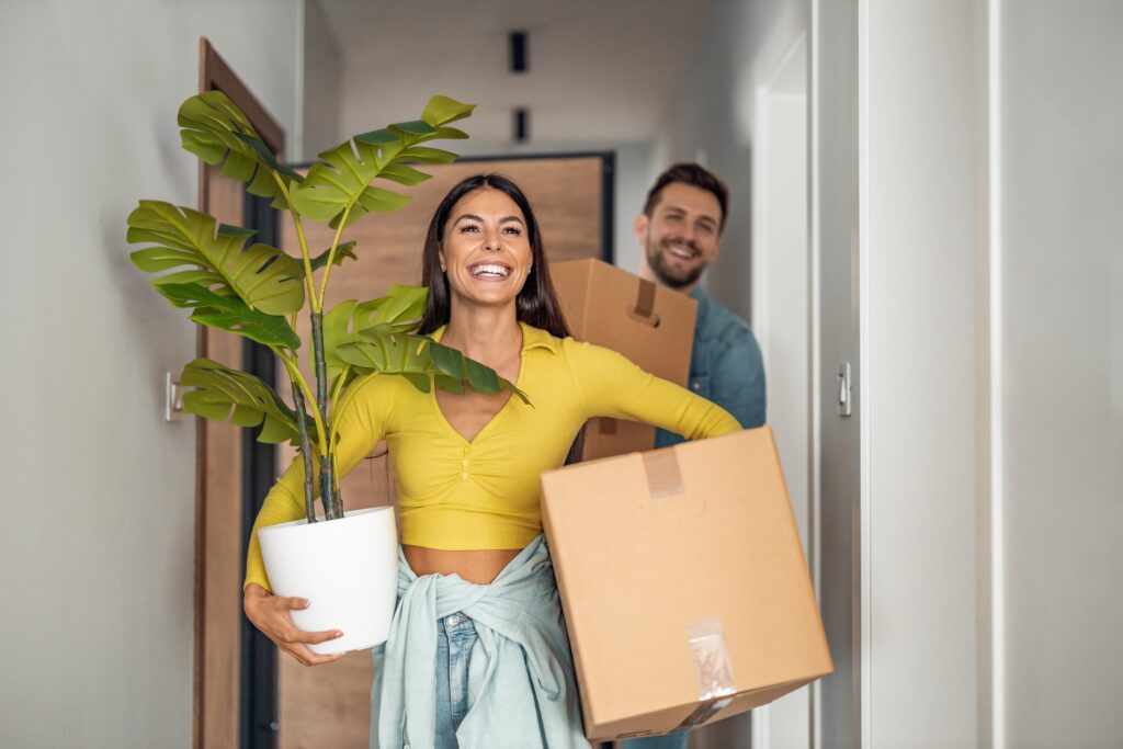 Woman holding plant and box with man behind her smiling