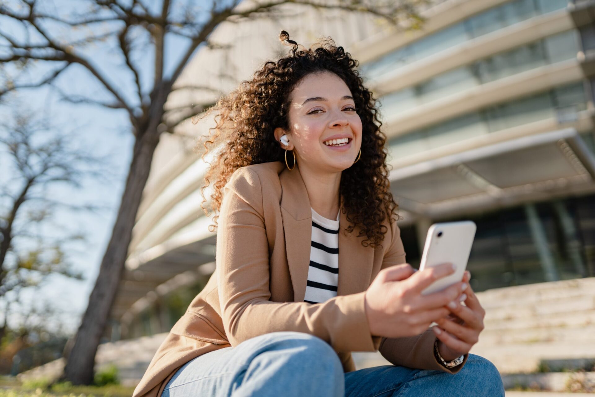 Woman sitting outside smiling while using smartphone