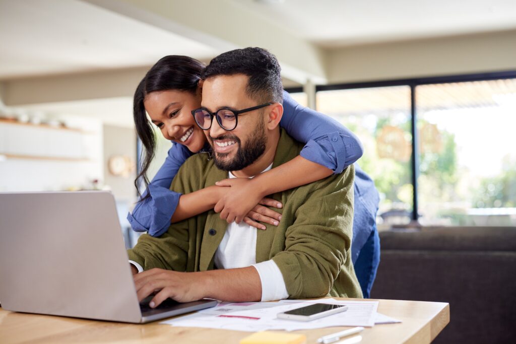 Man hugging woman from behind while they look at a laptop
